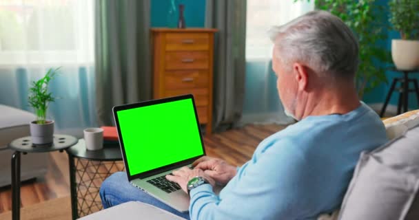 Mand hjemme sidder på en sofa, der arbejder på Green Mock-up Screen Laptop Computer. Fyr – Stock-video