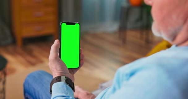 Senior Man at Home Gebruikt Green Mock-up Screen Smartphone. Ze zit op een bank in — Stockvideo