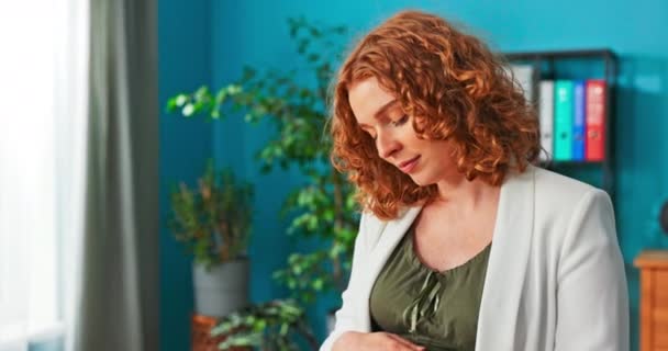 Mamá está sentada en la oficina vestida con una chaqueta blanca y pantalones cómodos de maternidad., — Vídeos de Stock