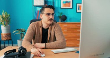 Genç, gülümseyen bir işadamı bilgisayarda çalışıyor, elinde fare tutuyor ve...