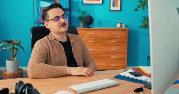Mannen bär glasögon med mustasch sitter på företagets kontor framför datorskärmen — Stockvideo