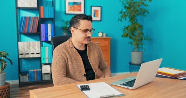 Wideo rozmowy przez kamerę internetową w biurze firmy, człowiek w okularach siedzi za biurkiem przed — Wideo stockowe
