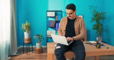 Ofiste çalışan şık giyimli bir adam kucağında dizüstü bilgisayarla oturuyor, hırslı.