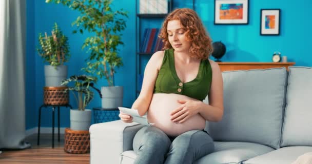 Szczęśliwa, opiekuńcza, troskliwa matka spoczywa na kanapie w salonie, dotyka dużego brzucha ciąży, czuje — Wideo stockowe