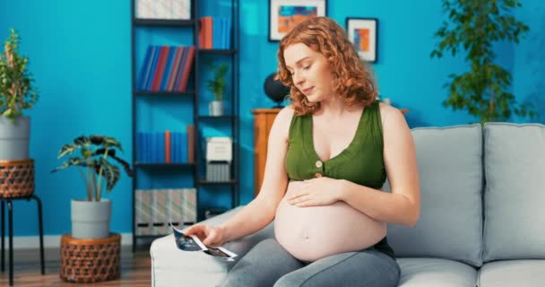 Feliz, cariñosa, madre reflexiva descansa en el sofá en la sala de estar, toca el vientre del embarazo grande, se siente — Vídeos de Stock