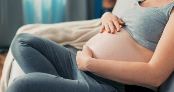 Close-up on profile of sitting pregnant women, living room scenery, girl dreamily touches her belly — Stock Video