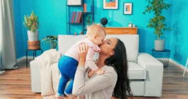 Sevgi dolu anne halıya oturur, bebeği sıkıca kavrar ve kollarını uzatarak kaldırır.,