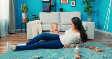 Uzun kahverengi saçlı güzel bir kadın oturma odasındaki halıya uzanmış, arkasında oturuyor.