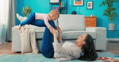 Çekici anne yatağın yanındaki halıya uzanmış, bacakları bükülmüş, kızı eğiliyor.