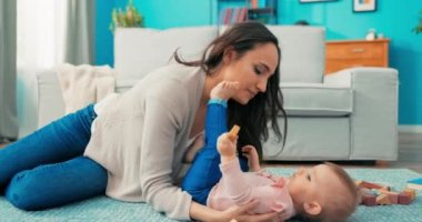 Güzel bir bayan, tatlı bir bebekle halıya oturur, küçük bir kız uzanır.