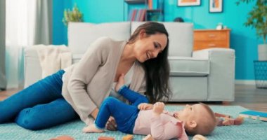 Güzel bir bayan, tatlı bir bebekle halıya oturur, küçük bir kız uzanır.