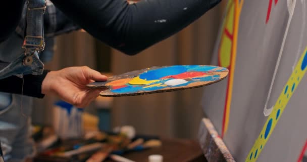 Close-up van houten palet met vlekken van verf, schilder staat dicht bij ezel met — Stockvideo