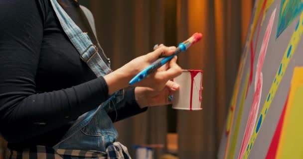 Ein Schüler in Jeans-Latzhose im Kunstunterricht malt ein abstraktes, modernes Bild mit Rot — Stockvideo