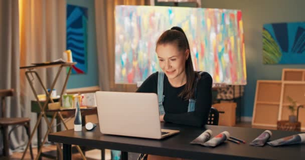 Um belo, jovem pintor trabalha em um salão, um estúdio de pintura, senta-se na mesa em — Vídeo de Stock