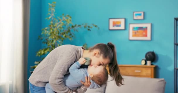 Felice donna sorridente trascorre del tempo in salotto tenendo il bambino tra le braccia, si sporge in avanti — Video Stock