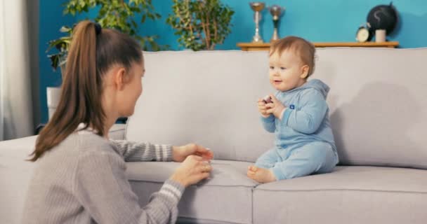 Un grazioso, adorabile, bel bambino vestito di blu bodysuit gira attraverso il divano, tiene — Video Stock