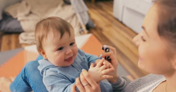 Een mooie vrouw zit op de vloer met gebogen benen houden baby, jongen is — Stockvideo