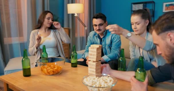 Pět přátel sedí kolem malého stolu s občerstvením a nápoji v obývacím pokoji doma — Stock video