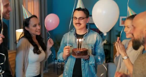 Fiesta de cumpleaños, chico está sosteniendo pastel con velas encendidas en las manos, soplar hacia fuera, amigos — Vídeo de stock