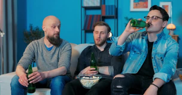 Tres amigos están sentados en el sofá en la sala de estar por la noche viendo su TV favorita — Vídeos de Stock