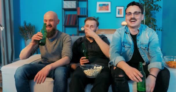 Tres amigos están sentados en el sofá en la sala de estar por la noche viendo su película favorita, — Vídeos de Stock