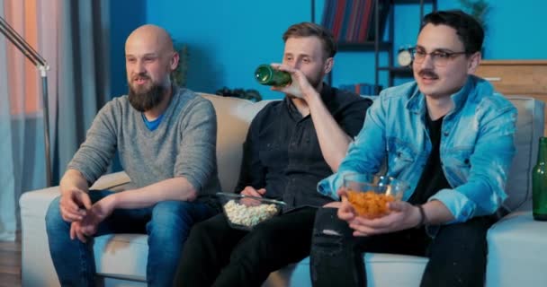 Amigos estão sentados no sofá na sala de estar à noite assistindo seu filme favorito, — Vídeo de Stock