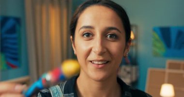 Yetenekli ressam, resme doğrudan bakıyor, elinde bir resim tutarak gülümsüyor.