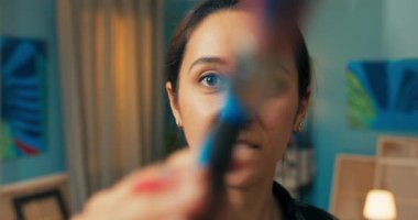 Yetenekli ressam, resme doğrudan bakıyor, elinde bir resim tutarak gülümsüyor.