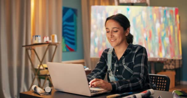 Mujer joven con sonrisa hace trabajo en el estudio de pintura, tienda de arte, charlando con clientes potenciales, da — Vídeo de stock