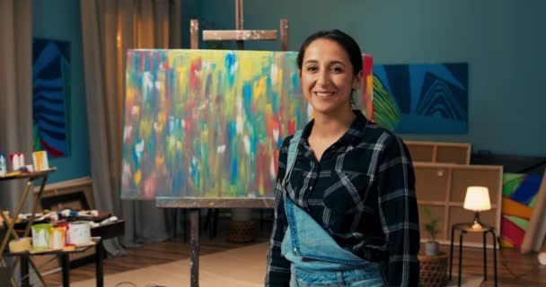 Femme portant des salopettes en denim, dans une main sale de la peinture tient un sourire au pinceau — Video