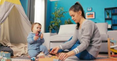 Genç sabırlı anne yerde tahta bloklar ve oyuncaklarla oynuyor.,