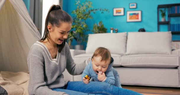 Een glimlachende, ontspannen vrouw zit op het tapijt van de woonkamer met haar jonge zoon die — Stockvideo