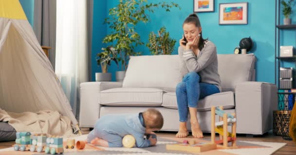 Mulher atraente faz uma pausa do trabalho de fim de semana assistindo o bebê, senta-se na sala de estar — Vídeo de Stock