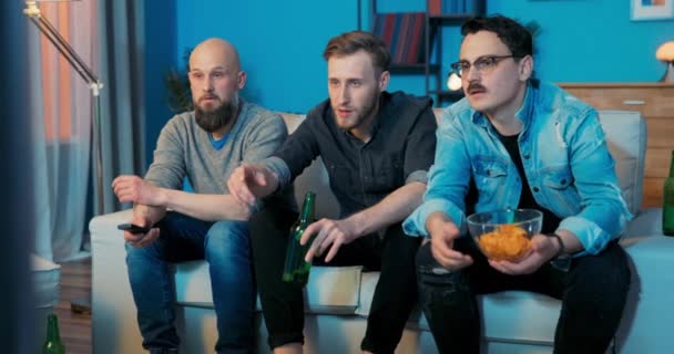 Noche de hombres frente a la televisión en el sofá, chicos bebiendo cerveza, comiendo palomitas de maíz hablando — Vídeos de Stock