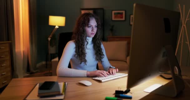 Krásná mladá dívka s kudrnaté vlasy sedí před obrazovce počítače ve večerních hodinách, — Stock video