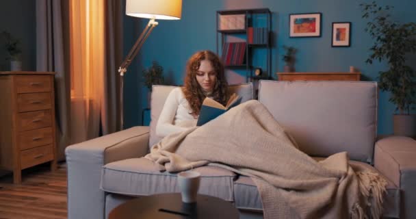 Cansada atractiva mujer se encuentra en el sofá en la noche cubierta con manta de descanso, relajante después del trabajo, — Vídeo de stock