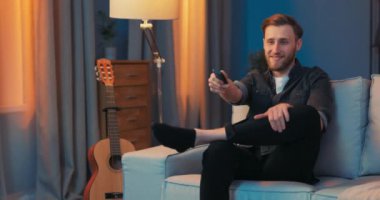 Genç bir adam akşamleyin oturma odasındaki kanepede dinleniyor.,