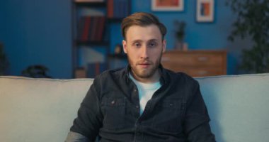 Şok olmuş bir adam oturma odasındaki koltukta oturuyor.