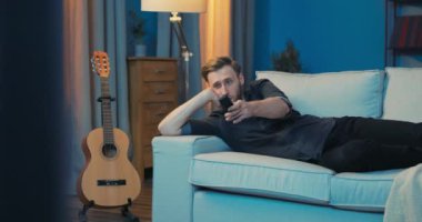 Yorgun adam yan yatmış, başını oturma odasındaki kanepeye dayamış.