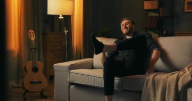 Mutlu bir adam işten dönüyor, gülümsüyor, keyfi yerinde, oturuyor.