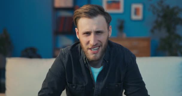 Un hombre guapo está sentado en el sofá tarde en la noche frente a la pantalla de TV — Vídeos de Stock