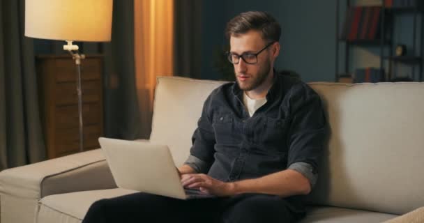 眼鏡をかけた大学生がリビングルームのソファの上に座っている — ストック動画