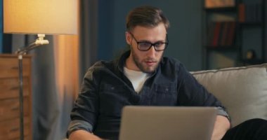 Meşgul işadamı, oturma odasında kanepede dizüstü bilgisayarını tutarak oturuyor.