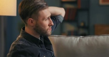 Sakallı bir üniversite öğrencisi akşamları oturma odasındaki kanepede oturur.