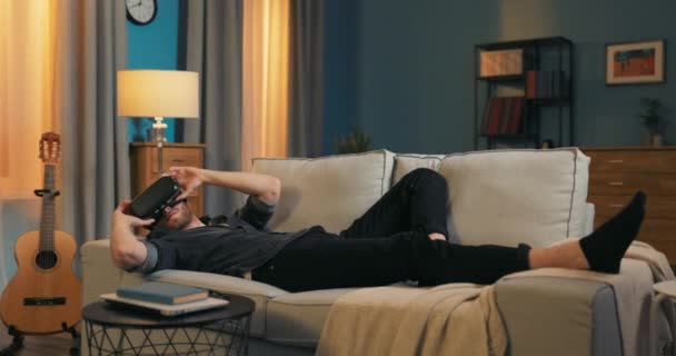 Homem relaxa no sofá após o trabalho com óculos de jogo vr em, realidade virtual, guy holds — Vídeo de Stock