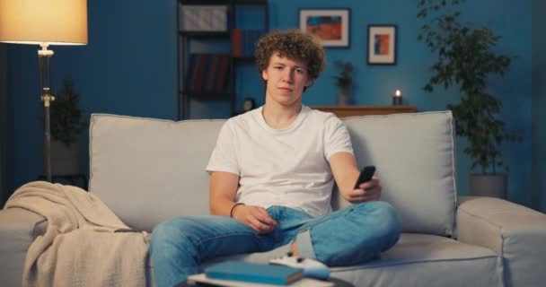 Підліток, брюнетка з кучерявим волоссям відпочиває на дивані у вітальні — стокове відео