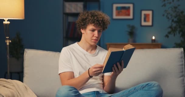 Handsome man with hair afro relaxes in homely attire while delving into book that is — Stock Video