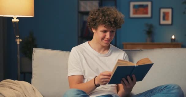 Sonriente hombre con pelo afro camiseta relaja en homely atuendo mientras ahonda en libro que — Vídeos de Stock