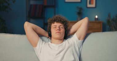 Adam kanepede dinleniyor, elleri başının arkasında, telsizde müzik dinliyor.