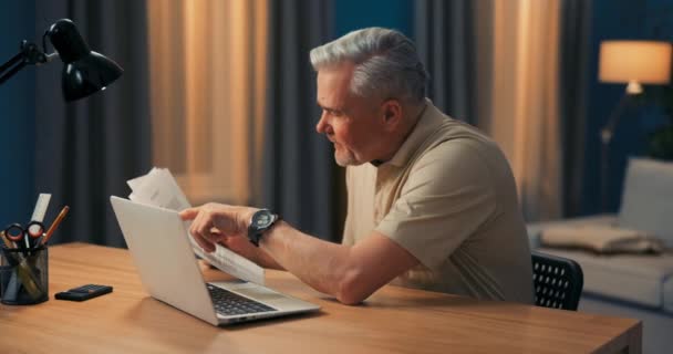Een foto van een oudere zakenman die achter een laptop zat met documenten. Man werkt op afstand in — Stockvideo